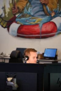 En ung mann sitter foran PC, med et veggmaleri i bakgrunnen.