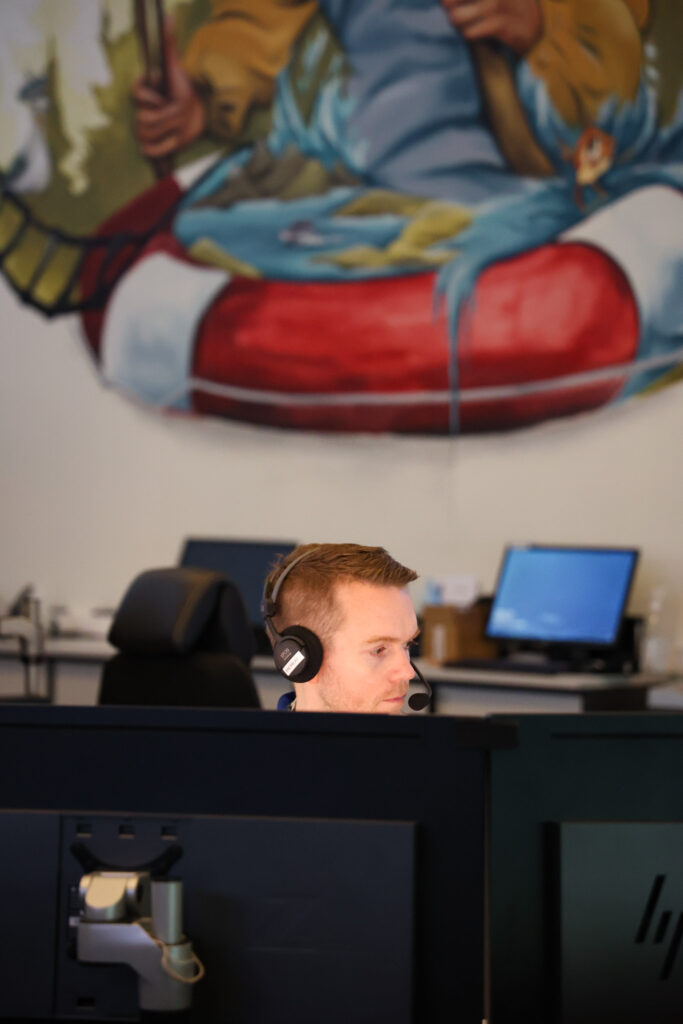 En ung mann sitter foran PC, med et veggmaleri i bakgrunnen. 