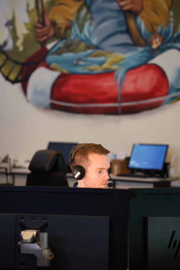 En ung mann sitter foran PC, med et veggmaleri i bakgrunnen.