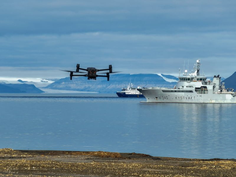 Kystvaktskip, drone og ekspedisjonsskip ligger i en fjord på Svalbard