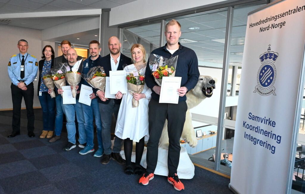 En gruppe mennesker står på rekke og rad og holder diplomer og blomsterbuketter