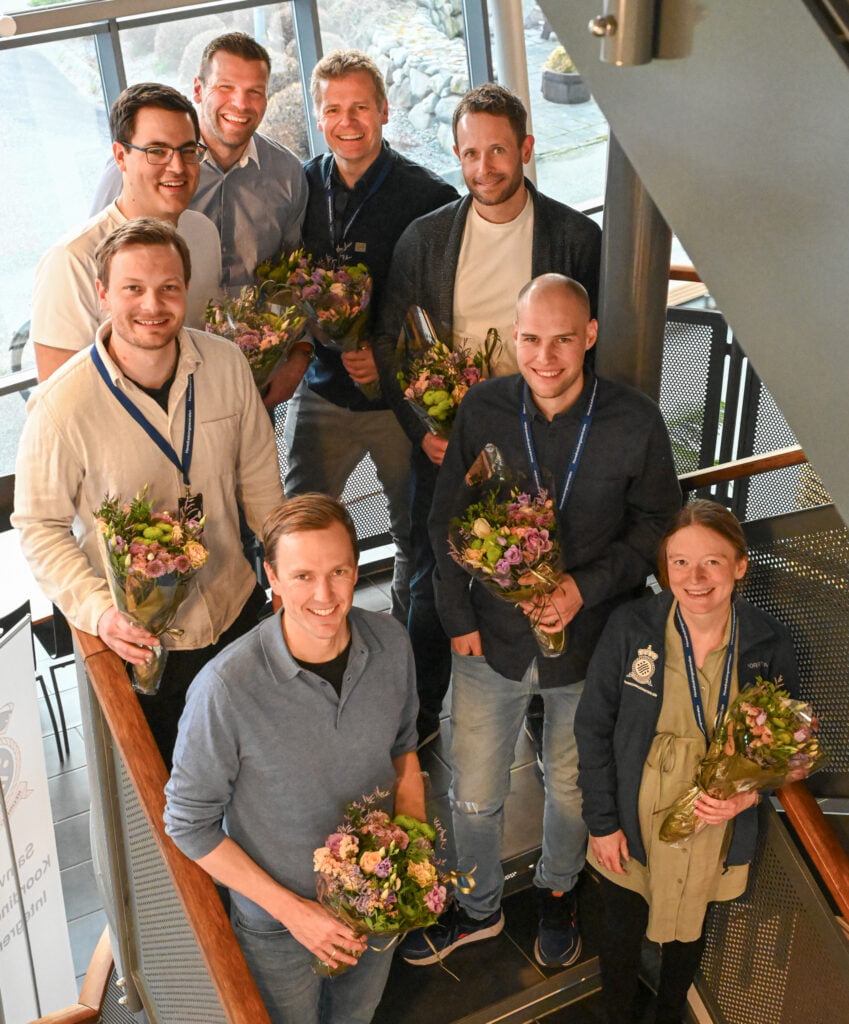 8 glade mennesker med hver sin blomsterbukett