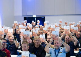 Mennesker i sal holder opp en publikasjon mens de smiler.